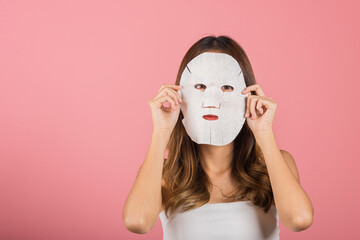 Portrait Asian young woman applying cosmetic paper sheet mask on her face studio shot isolated on pink background, beautiful female with natural makeup cosmetic mask, beauty skin care concept