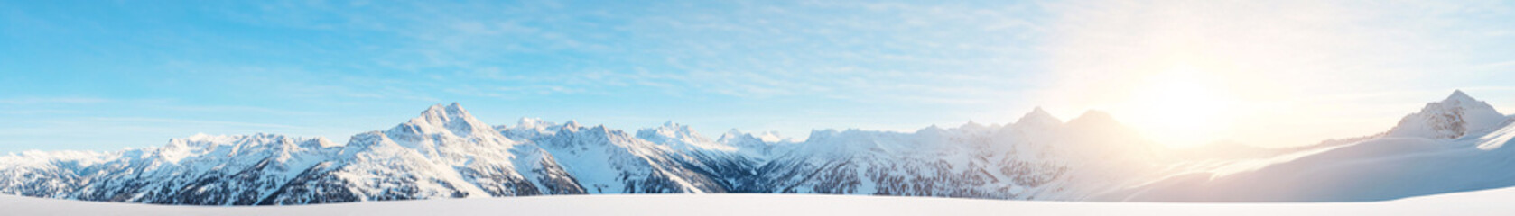Obraz premium A breathtaking panoramic view of a vast mountain range covered in pristine snow. The jagged peaks rise sharply against a clear blue sky, with layers of snow glistening under the bright sunlight. The