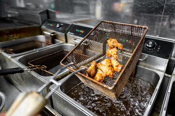 Close-up of fried chicken being lifted from a deep fryer in a commercial kitchen, showcasing the...
