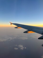 Obraz premium Breathtaking view of white wing of aircraft flying in blue sky over colorful fluffy cumulus clouds in sunset