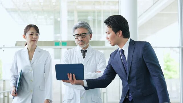 ビジネスマンから説明を受ける白衣の医師・研究者