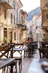 Under the warm sun, a quaint café in Nafplio features empty tables lining the cobblestone alley, hinting at delightful moments shared over coffee and pastries.