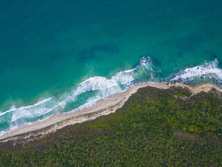 Aerial view of turquoise waves crashing on a sandy beach surrounded by lush greenery in a tranquil...