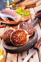 Cooked fried fish cutlets in a plate, on a light wooden table.