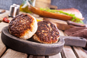 Cooked fried fish cutlets in a plate, on a light wooden table.