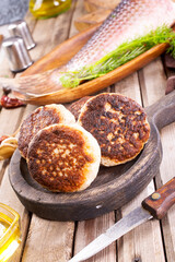 Cooked fried fish cutlets in a plate, on a light wooden table.