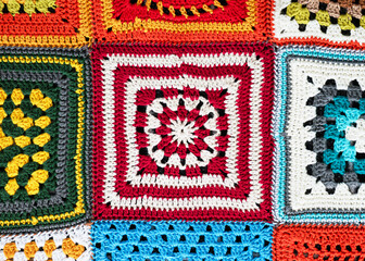 Fragment of blanket made of granny Square crocheted with red, white, yellow, green, blue and orange yarn with different motifs. Handmade crocheting, needlework and handicraft concept