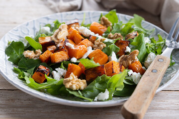 Pumpkin salad with arugula, walnuts and feta cheese on wooden table. Autumn healthy food