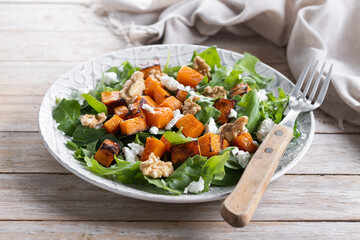 Pumpkin salad with arugula, walnuts and feta cheese on wooden table. Autumn healthy food