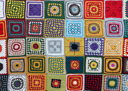 View from above of beautiful multi colored plaid make from crochet granny squares with different motifs. Handmade crocheting, needlework and handicraft concept. 