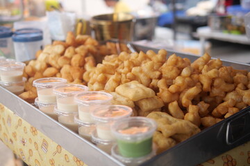 Crispy fried dough pieces served with dipping sauces in plastic cups, displayed at a street food stall for sale.
