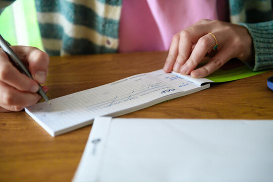 Paris, France - Sep 21, 2024: A woman writes a bank cheque from CCF Banque France, carefully noting the recipient and amount on a wooden table - former HSBC France bank