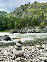 Round stones are balanced on top of each other, against the backdrop of a flowing river and rugged mountains, embodying the concept of natural balance. Altai, Russia