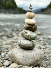 Round stones are stacked atop one another, set against the backdrop of a river and mountainous terrain, serving as a conceptual symbol of natural equilibrium.