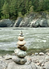 Smooth round stones are carefully balanced on top of each other, against the scenic view of a flowing river and rugged mountains, epitomizing the concept of natural balance.
