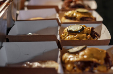 Freshly made cheeseburgers in takeout containers, topped with melted cheese and pickles, ready for delivery or serving in a fast food restaurant setting