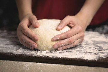 Woman's hands holding dough over kitchen board, warm photo of home baking process.	