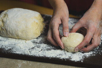 Women's hands forming buns of dough on a kitchen board, warm photo of the home baking process.	