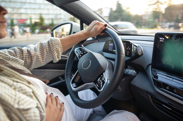 A pregnant young woman is driving a car. Hands on the wheel.