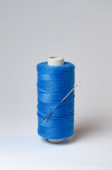 One single blue thread spool with needle on white background