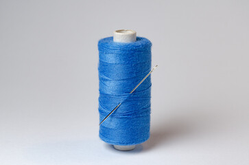 One single blue thread spool with needle on white background