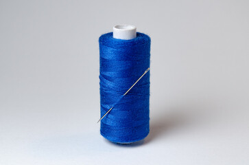 One single dark blue thread spool with needle on white background