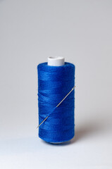 One single dark blue thread spool with needle on white background