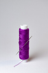 One single purple thread spool with needle on white background