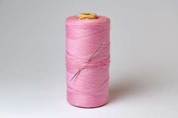 One single pink thread spool with needle on white background