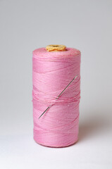 One single pink thread spool with needle on white background