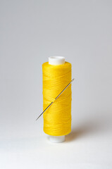 One single yellow thread spool with needle on white background