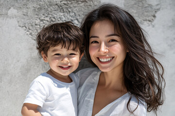 Mixed racial young mother and cute daughter smiling and interacting in front of a plain background, dressed in simple  clothes, captured in a family photo portrait shoot showcasing their joyful bond