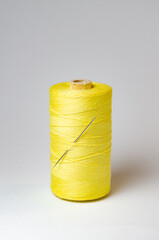 One single yellow thread spool with needle on white background