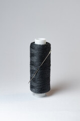 One single black thread spool with needle on white background