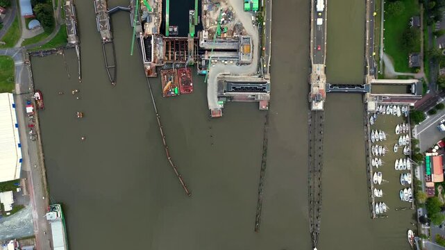 Topdown Aerial drone 4K film of large cargo container ship carrier in lock sluice complex under construction in Brunsb&uuml;ttel Germany at entrance of nord ostsee kanal or Kiel canal with small sailboat 