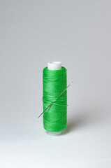 One single green thread spool with needle on white background