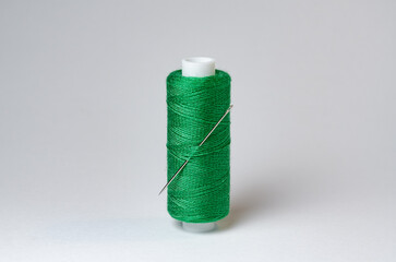 One single green thread spool with needle on white background