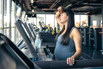 Obraz premium Pregnant woman on a treadmill in the gym. Healthy sports lifestyle.