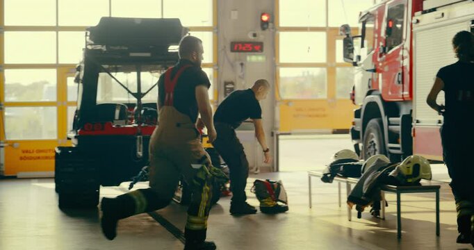 Firefighter Team, Made Up of Men and a Female Crew Members, Quickly Mobilizes. Young Man Uses the Pole as They Gear Up in the Garage. Group Gets Into the Fire Truck, Ready for an Emergency Response