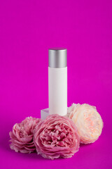Plastic white tube for cream or lotion. Skin care or sunscreen cosmetic with fake flowers on purple background.