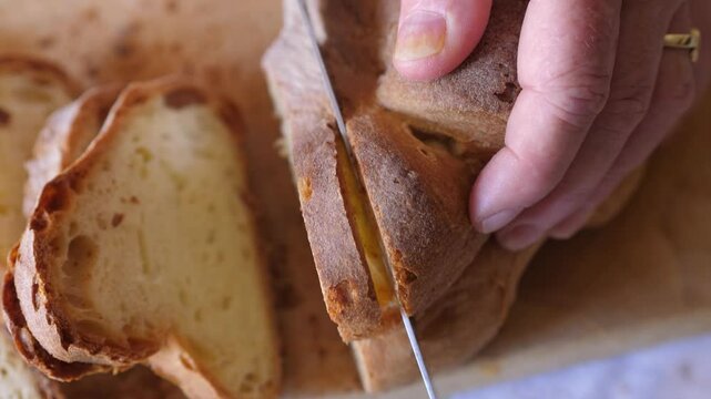 Top-down close-up of a hand slicing the famous Matera bread with a knife, preparing it for lunch. Showcases the texture and quality of the bread.