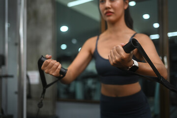 Young fit woman in sportswear lifting weights using a cable machine at the gym