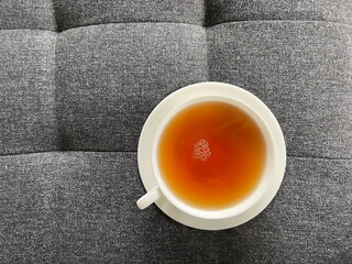 Teezeit - weiße Porzellantasse mit Schwarztee auf grauem Polstermöbel
