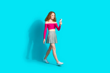Full size photo of nice young girl walk use phone wear top isolated on teal color background