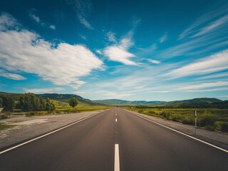 Open road stretching through green valleys under a blue sky