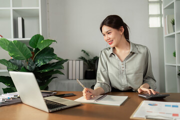 Young Professional Woman Working at Home Office Desk with Laptop, Notebook, and Calculator