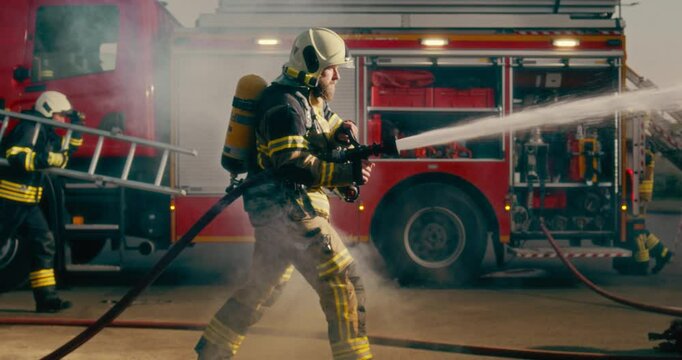 Caucasian Firefighter Sprays Water From His Hose, Extinguishing Flames to Keep the Situation Under Control. Fire Truck Stands in the Background as He Works to Protect Lives and Property