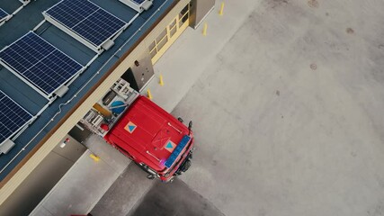Aerial Footage of a Fire Truck Exiting a Fire Department with Modern Solar Panels Installed on the Roof. Firefighters Responding to an Emergency Call. Team Drive Off to Handle a Critical Situation