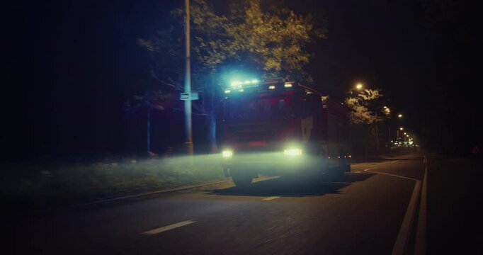 Fire Truck with Flashing Emergency Lights Speeds Down a City Street at Night, Responding to an Urgent Call. Vehicle Cuts Through the Darkness, Racing Towards the Accident Scene. Follow Footage