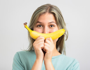 Funny young womand holding a banana in front of her face.